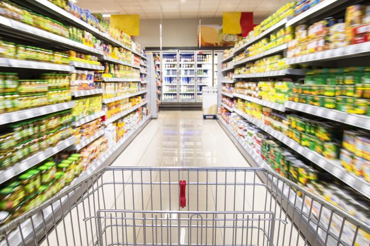 Ein leerer Einkaufswagen zwischen Regalreihen im Supermarkt.